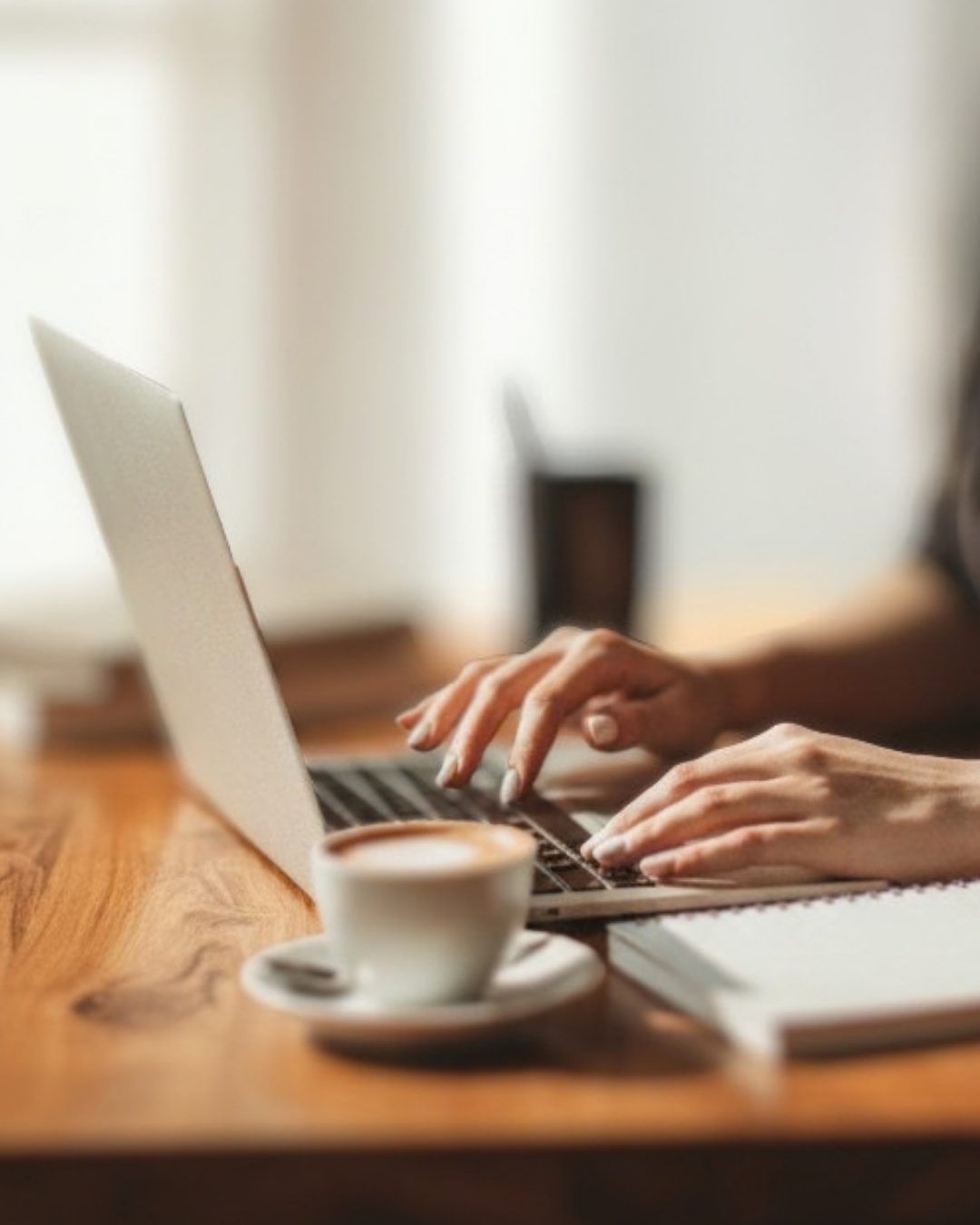 Mãos digitando no notebook com café ao lado