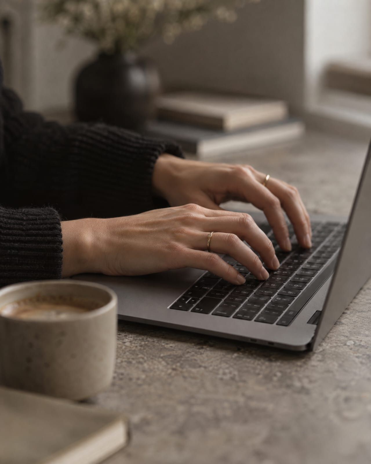 Mãos digitando no notebook com café ao lado